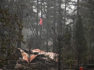 Sebuah bendera Amerika terlihat di atas properti yang terbakar dalam Kebakaran Dixie Fire di daerah Air Terjun India di Plumas County, California (26/7/2021). Api menghanguskan beberapa tempat tinggal di daerah tersebut. (AFP/Robyn Beck)