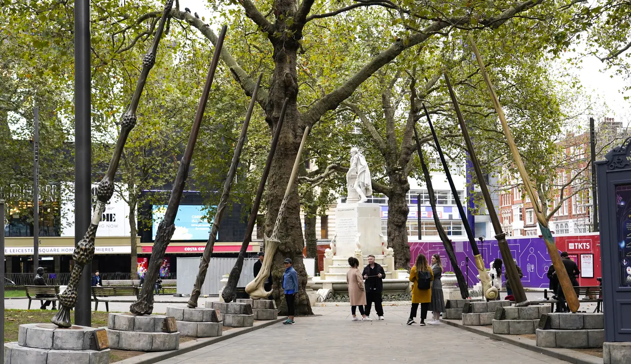 Orang-orang berjalan di bawah tongkat raksasa untuk peringatan 20 tahun film Harry Potter and the Philosopher's Stone di Leicester Square, London, Rabu (13/10/2021). Instalasi terdiri dari sembilan tongkat setinggi 15 kaki yang mewakili sembilan karakter kunci dari film. (AP Photo/Alberto Pezzali)