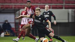 Bek PSV Eindhoven, Timo Baumgartl (kanan) berebut bola dengan striker Olympiacos, Ahmed Hassan pada laga leg pertama babak 32 Besar Liga Europa 2020/2021 di Georgios Karaiskakis Stadium, Piraeus (18/2/2021). Timo Baumgartl didatangkan PSV dari VfB Stuttgart pada awal musim 2019/2020 dengan nilai transfer 12 juta euro atau kini setara Rp199 miliar. Setelah dua musim membela PSV, sejak awal musim 2021/2022 ia dipinjamkan ke Union Berlin selama dua musim hingga akhir musim 2022/2023. (AFP/Aris Messinis)