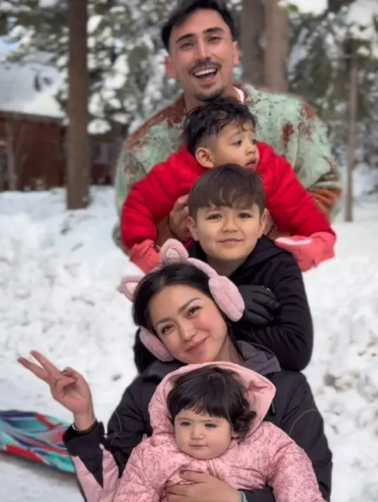 Jessica Iskandar mengenakan jaket hitam saat main salju bersama ketiga anaknya dan suaminya. Semakin cute dengan penutup telinga warna pink. [@inijedar]