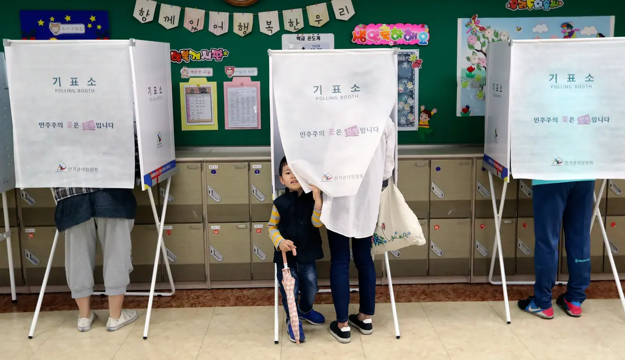 Seorang anak mengintip dari bilik suara saat ibunya menggunakan hak suara untuk memilih presiden baru di sebuah TPS di Seoul, Selasa (9/5). Hari ini, warga Korsel mulai untuk memilih presiden baru setelah pemakzulan Park Geun-hye. (AP Photo/Lee Jin-man)