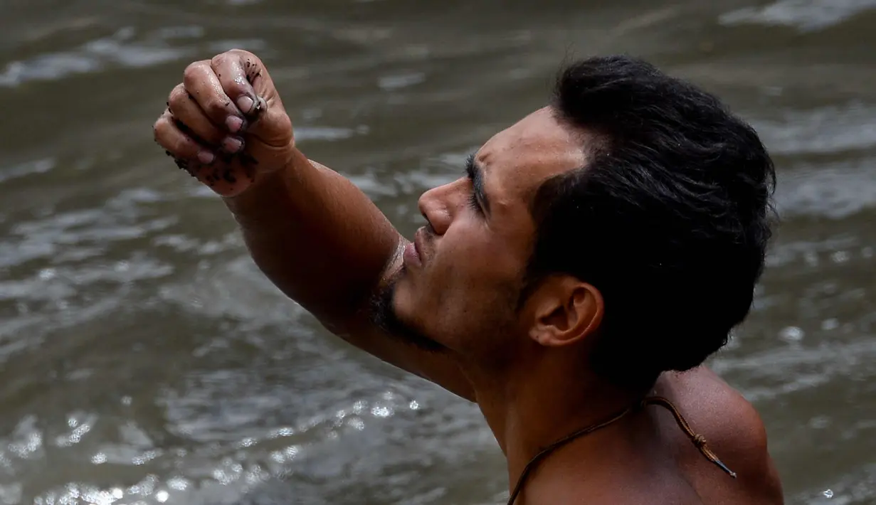 Seorang pria mengamati benda yang ditemukannya di saluran pembuangan limbah di Sungai Guaire, di Caracas, (1/2). Puluhan warga mencari logam atau tembaga setiap hari di Sungai Guaire. (AFP Photo/Federico Parra)