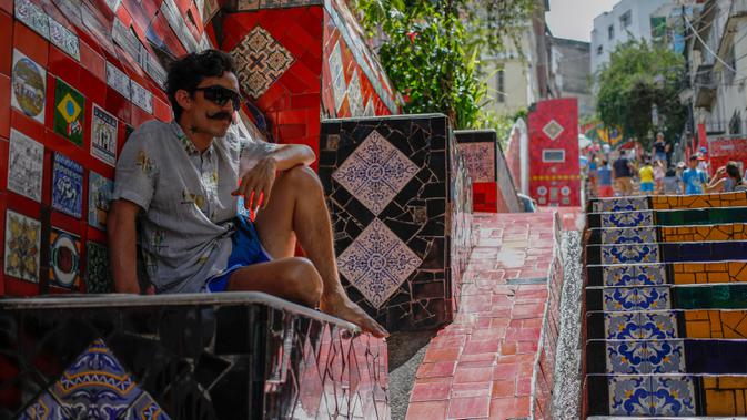Seorang pria duduk anak tangga yang terkenal dengan nama Selaron Steps atau Escadaria Selarón di Rio de Janeiro, Brasil pada 9 Desember 2019. Escadaria Selaron merupakan 250 anak tangga sepanjang 125 meter dengan dua ribuan ubin berwarna-warni. (Photo by David GANNON / AFP)