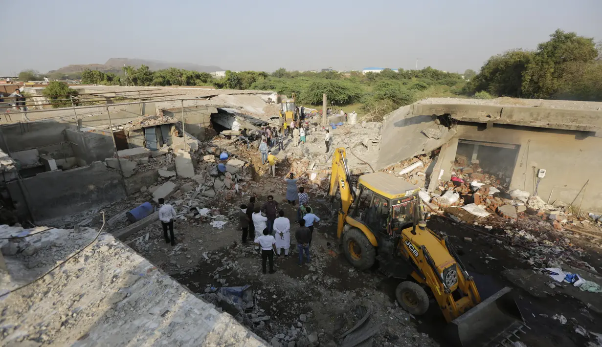 Orang-orang berdiri di lokasi kebakaran di sebuah pabrik di kawasan industri di pinggiran Ahmedabad, India (4/11/2020). Menurut pejabat setempat, puluhan orang tewas ketika sebagian gudang bahan kimia runtuh setelah terjadi ledakan dahsyat. (AP Photo/Ajit Solanki)