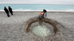 Petugas dibantu keluar dari  kawah misterius berisi air payau yang muncul di Pantai Lido, Nice, Prancis, Kamis (1/2). Pihak berwenang mengatakan, lubang yang mulai terbentuk pada Rabu itu tidak menimbulkan bahaya bagi keamanan publik. (VALERY HACHE/AFP)
