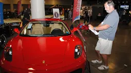 Pengunjung mengambil gambar mobil Ferrari F430 yang dipamerkan oleh Auctions America di Florida, 31 Maret 2017. Mobil berwarna merah menyala produksi 2007 itu pernah digunakan oleh Presiden AS, Donald Trump, selama empat tahun. (LEILA MACOR/AFP)