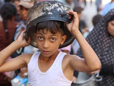 Seorang anak laki-laki Palestina mengantri untuk menerima jatah makanan, yang ditawarkan oleh sebuah badan amal, di kamp pengungsi Al-Shati di Gaza pada 17 Oktober 2024. (Omar AL-QATTAA/AFP)