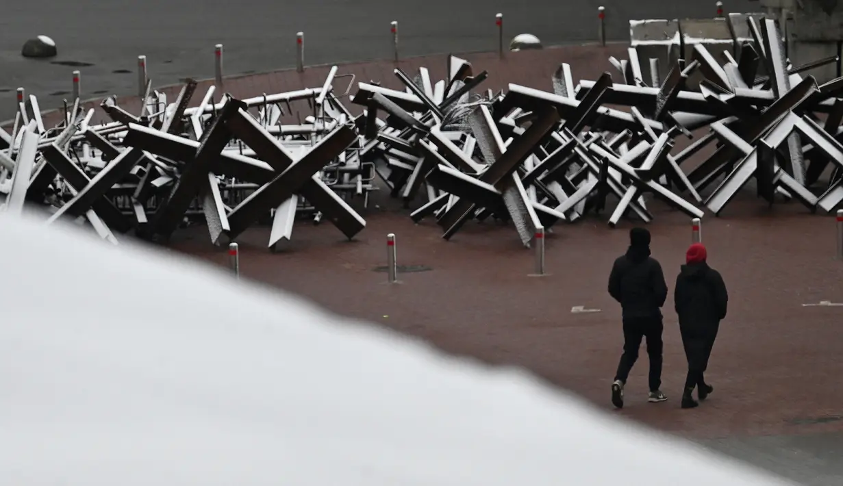 Pejalan kaki melewati konstruksi antitank yang tertutup salju setelah salju pertama turun musim ini di Kiev, Ukraina, 17 November 2022. Salju pertama musim ini turun di tengah invasi Rusia ke Ukraina. (Sergei SUPINSKY/AFP)