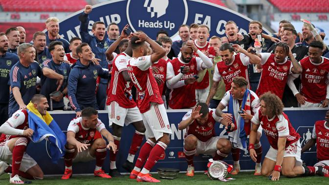 Striker Arsenal, Pierre-Emerick Aubameyang (tengah) menjatuhkan trofi saat merayakan gelar juara Piala FA usai mengalahkan Chelsea pada pertandingan final Piala FA di stadion Wembley, Minggu (2/8/2020).  Aubameyang terlihat kaget sambil memegang kepalanya saat trofi terjatuh. (Adam Davy/Pool via AP)