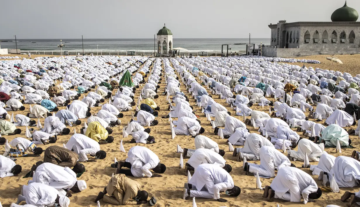 Pengikut komunitas Layene Senegal melaksanakan salat Ied selama perayaan Tabaski (Idul Adha) di lingkungan populer Yoff di Dakar, Rabu (21/7/2021). Bendera putih kecil yang tertancap di atas pasir pantai Yoff terpasang sebagai penanda jaga jarak antar jemaah. (JOHN WESSELS / AFP)