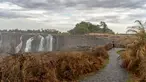 Seorang turis melihat Air Terjun Victoria yang megah di Zimbabwe (13/11/2019). Serangkaian gelombang panas telah mengeringkan sebagian besar vegetasi di sekitar situs warisan dunia UNESCO berukuran 108 meter dan lebar hampir 2 km dalam kekeringan parah. (AFP/Zinyange Auntony)
