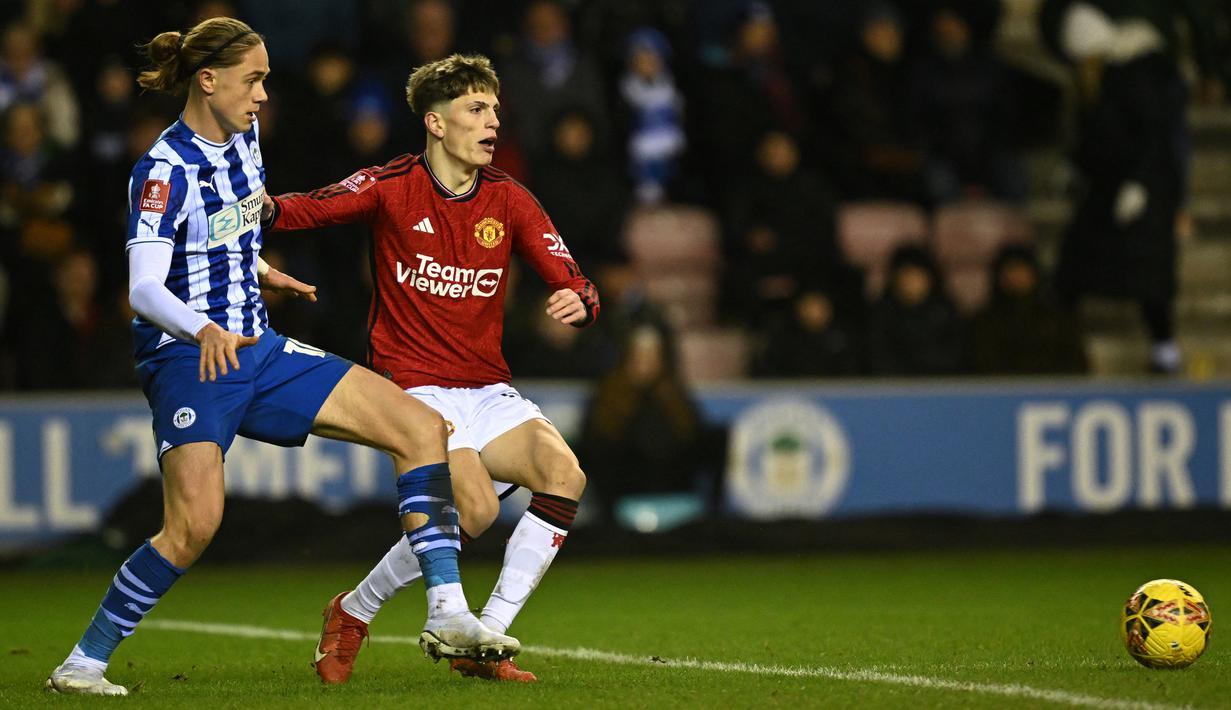 Gelandang Manchester United #17 Alejandro Garnacho (kanan) bersaing dengan gelandang Wigan Athletic #10 Thelo Aasgaard pada laga putaran ketiga FA Cup 2023/2024 di DW Stadium, Selasa (9/1/2024) dini hari WIB. (Paul ELLIS / AFP)
