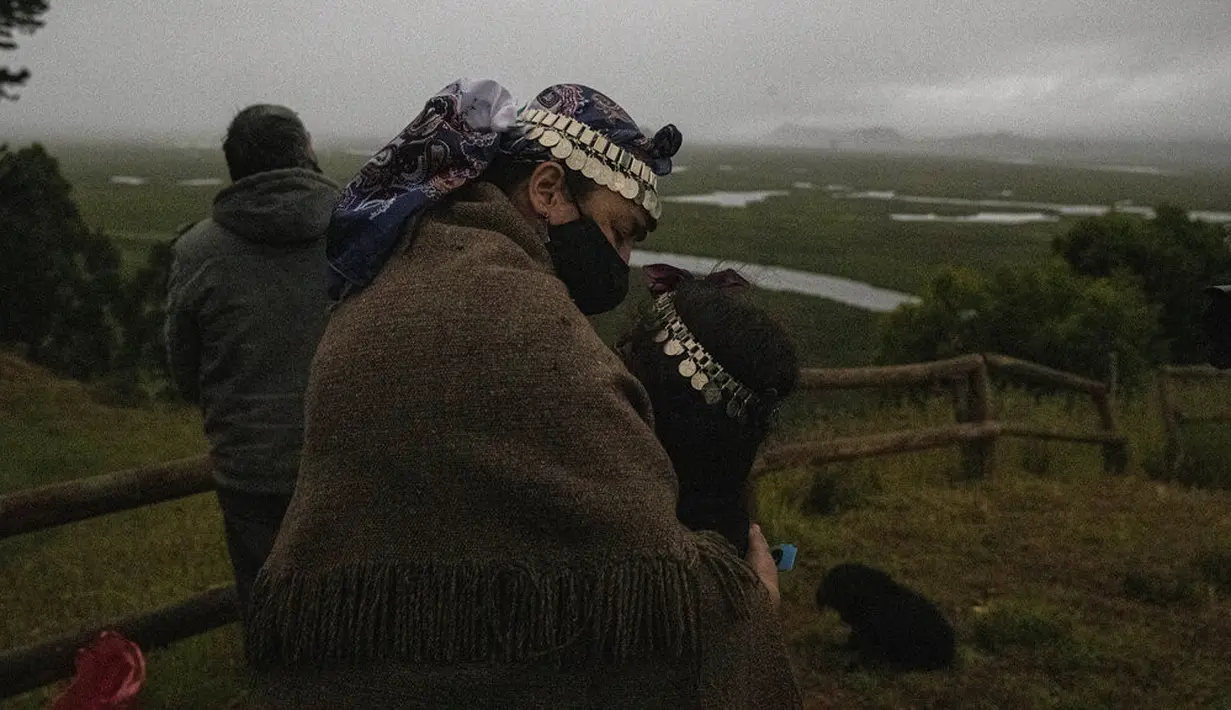 Seorang nenek Adat Mapuche memeluk cucunya saat gerhana matahari total di Carahue, La Araucania, Chile, Senin (14/12/2020). Gerhana matahari total terlihat dari Chile dan wilayah Patagonia utara Argentina. (AP Photo/Esteban Felix)