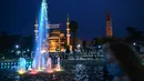 Sepasang suami istri berjalan melewati air mancur pada hari pertama bulan puasa Muslim Ramadhan di Sultanahmet Square dengan latar belakang Masjid Biru, di Istanbul (13/4/2021). (AFP Photo/Ozan Kose)