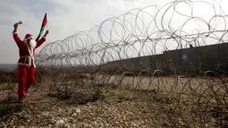 Seorang pengunjuk rasa berkostum Santa Claus berteriak-teriak di desa Tepi Barat Bilin dekat Ramallah, Jumat (23/12). Pengunjuk rasa menentang pembangunan tembok pembatas di Israel. (REUTERS/Mohamad Torokman)