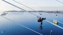 Pekerja menghilangkan es dari kabel Jembatan Russky yang melintasi Selat Bosphorus Timur di Vladivostok, Rusia, Senin (30/11/2020). Banyak di antara pepohonan, mobil, jalan, dan kabel listrik yang tertutup lapisan es tebal rusak karena beban. (AP Photo/Aleksander Khitrov)