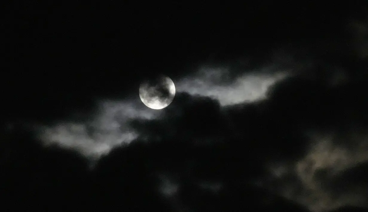 Bulan purnama terlihat pada balik awan di Johannesburg, Afrika Selatan, 14 Juni 2022. Fenomena ini disebut juga sebagai Strawberry Supermoon karena terjadi pada saat panen strawberry. (AP Photo/Themba Hadebe)