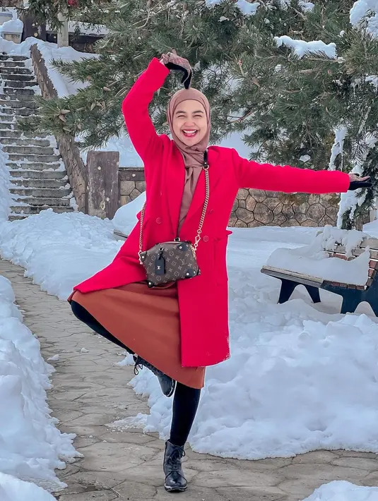 Ria Ricis memakai outerwear mantel warna merah untuk menghangatkan tubuhnya di tengah salju sekaligus menjadi gaya pernyataan yang bold. (Foto: Instagram @teukuryantr)