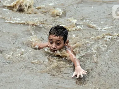 Seorang anak berenang di Kali Ciliwung yang meluap, Kebon Pala, Jatinegara, Jakarta Timur, Minggu (31/10/2021). Aliran Kali Ciliwung yang meluap akibat hujan di kawasan hulu dimanfaatkan anak-anak untuk berenang meski membahayakan keselamatan. (merdeka.com/Iqbal S. Nugroho)