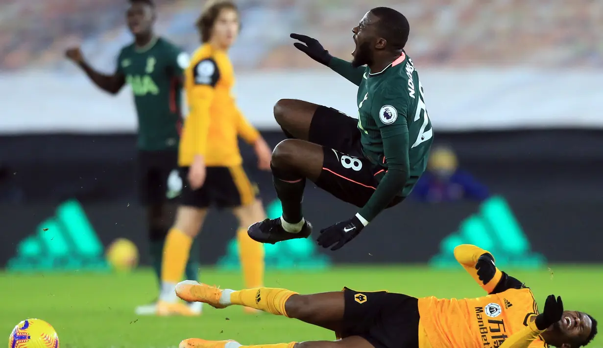 Gelandang Tottenham Hotspur, Tanguy Ndombele (atas) dilanggar bek Wolverhampton Wanderers, Nelson Semedo dalam laga lanjutan Liga Inggris 2020/21 pekan ke-15 di Molineux Stadium, Minggu (27/12/2020). Tottenham bermain imbang 1-1 dengan Wolves. (AFP/Lindsey Parnaby/Pool)