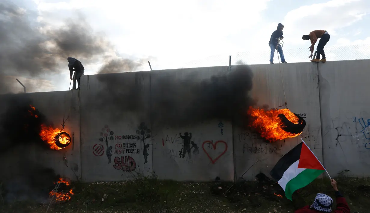 Pengunjuk rasa Palestina memanjat tembok pemisah dengan Israel saat aksi di desa Tepi Barat Bilin dekat Ramallah, Jumat (17/2). Aksi tersebut untuk memperingati 12 tahun protes mereka atas tembok pemisah tersebut. (AP Photo / Majdi Mohammed)