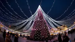 Pengunjung berjalan di sekitar pohon Natal raksasa yang menerangi Alun-Alun Katedral di Vilnius, Lithuania, 5 Desember 2017. Di sisi lain, pohon Natal tampak seperti bintang raksasa yang ada di bumi jika dilihat dari ketinggian (AP Photo/Mindaugas Kulbis)