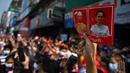 Seorang pengunjuk rasa memegang poster dengan gambar pemimpin terpilih Aung San Suu Kyi (kanan) yang ditahan dan presiden Win Myint saat demonstrasi menentang kudeta militer di Yangon, Myanmar pada Sabtu (6/2/2021).  Ribuan orang turun ke jalan-jalan untuk melawan kudeta. (YE AUNG THU / AFP)