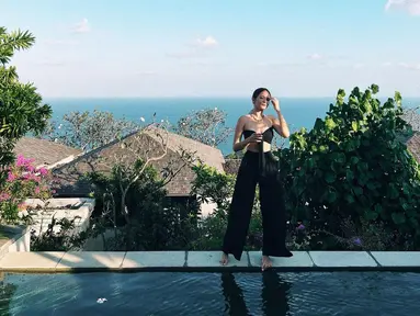 Berpose di pinggir kolam renang, Enzy Storia terlihat memesona dan seksi mengenakan bandeau tie crop top berwarna hitam yang dipadu padakankan dengan pallazo kasual warna senada. (Instagram/enzystoria)