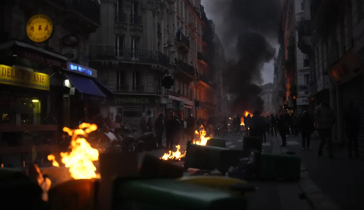 Para pengunjuk rasa berbaris di belakang tong sampah saat mereka berdemonstrasi setelah Presiden Prancis Emmanuel Macron mencoba meredakan ketegangan dalam pidato yang disiarkan di televisi, di Paris, Senin (17/4/2023). (AP Photo/Thibault Camus)