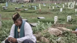 Seorang pembaca doa saat duduk di dekat makam jenazah terkait Covid-19 di TPU Tegal Alur, Jakarta, Kamis (14/1/2021). Hingga saat ini tercatat sebanyak 4.500 jenazah terkait Covid-19 telah dimakamkan di blok muslim TPU Tegal Alur. (merdeka.com/Iqbal S. Nugroho)