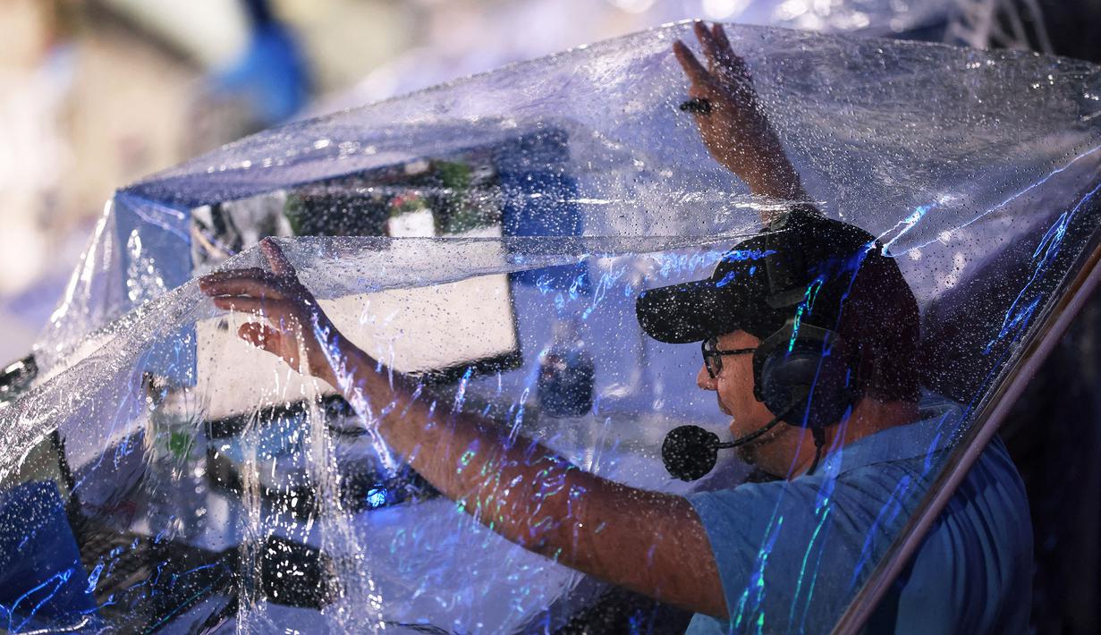 Seorang komentator olahraga menutupi dirinya dengan selembar plastik untuk melindungi diri dari hujan dalam nomor pakaian individu berkuda selama Olimpiade Tokyo 2020 di Taman Berkuda di Tokyo pada 30 Juli 2021. (AFP/Behrouz Mehri)