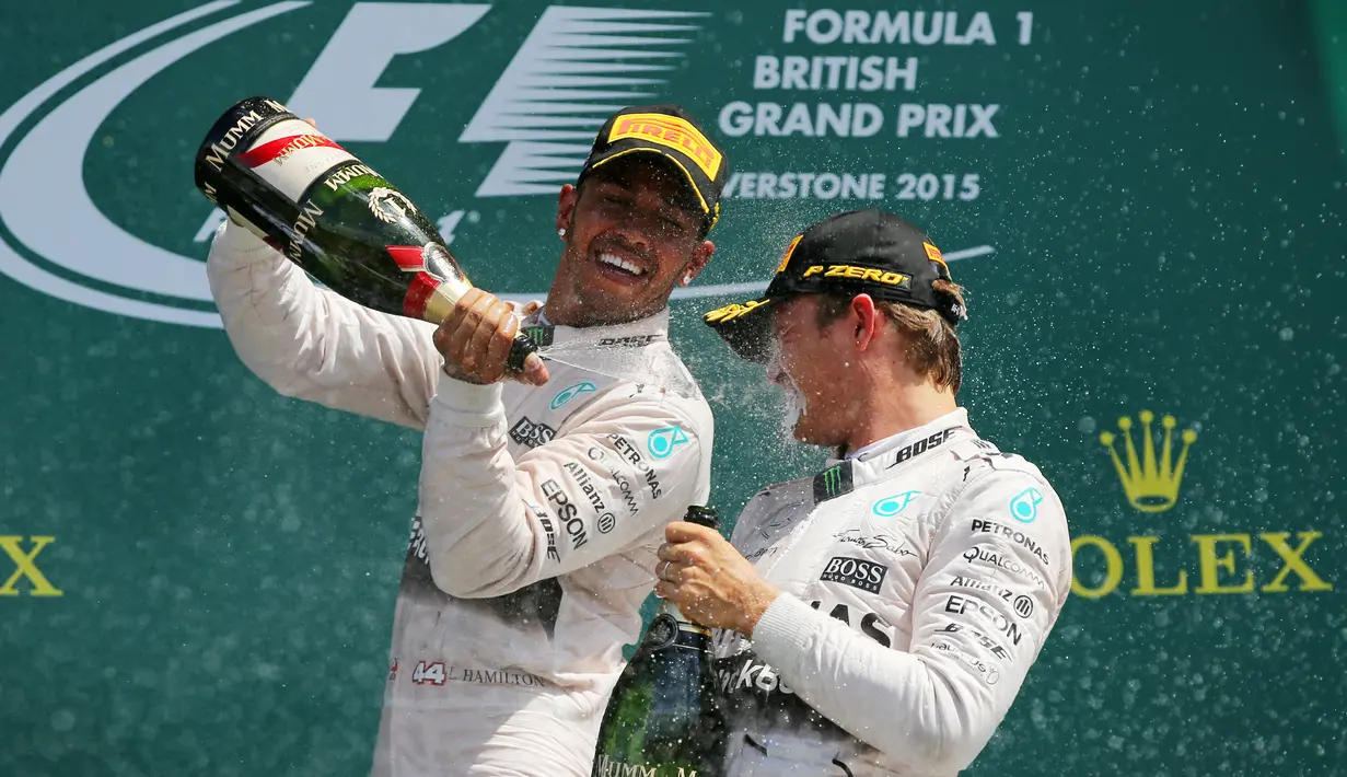 Pembalap Formula 1, Lewis Hamilton (kiri) menyemprotkan sampanye ke teman satu timnya, Nico Rosberg usai berlaga di Grand Prix Formula 1 Silverstone di Inggris, (5/7/2015). (Reuters/Paul Childs)