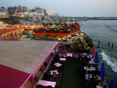 Keluarga Palestina menikmati makanan di sebuah restoran di sepanjang pantai di Kota Gaza (10/6/2019). Pergi ke restoran di dekat pantai merupakan opsi bagi warga Palestina untuk menikmati suasana alam. (AFP Photo/Mohammed Abed)