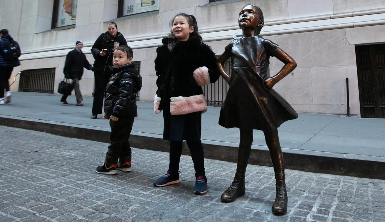 Anak-anak berpose dengan patung Fearless Girl di lokasi barunya di depan bursa efek New York, Selasa (11/12). Kini patung perunggu yang sempat menimbulkan kontroversi itu mendapatkan rumah baru yang lebih permanen. (AP/Mark Lennihan)
