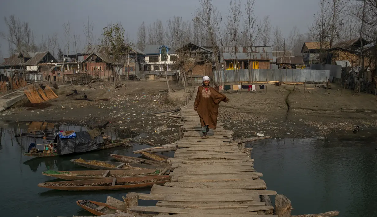 Seorang wanita Kashmir melintasi jembatan kayu di sebuah desa di pinggiran Srinagar, Kashmir yang dikuasai India (30/11/2021). Warga Kashmir menggunakan tungku tradisional ini untuk menghangatkan diri selama bulan-bulan musim dingin yang parah. (AP Photo/Dar Yasin)