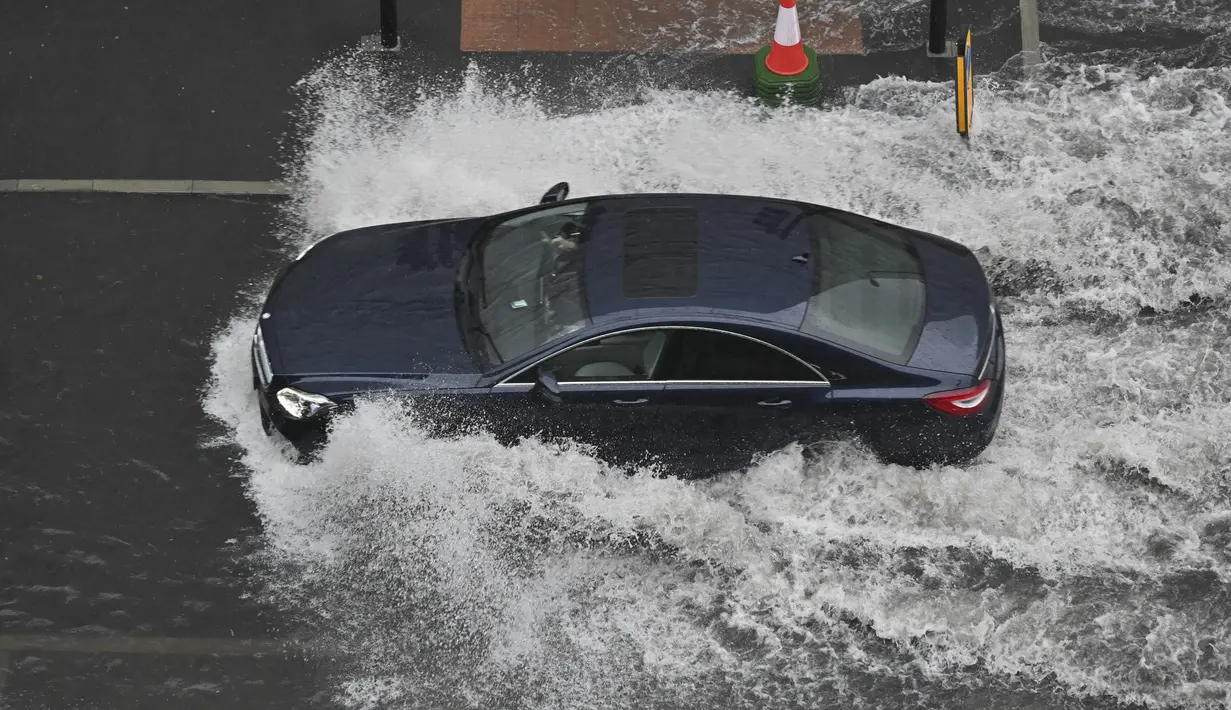 Sebuah mobil melintasi jalan yang banjir saat hujan lebat di distrik The Nine Elms London (25/7/2021). Bus dan mobil terjebak banjir ketika jalan-jalan di London banjir pada hari Minggu, ketika badai petir berulang kali melanda ibu kota Inggris. (AFP/Justin Tallis)