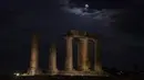 Supermoon terlihat di atas kuil Apollo, Yunani, Selasa (7/4/2020). Fenomena dimana bulan berada pada titik terdekat dengan bumi ini merupakan penampakan supermoon terbesar di tahun 2020. (AP Photo/Petros Giannakouris)