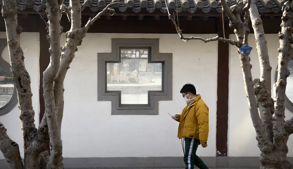 Seorang pria mengenakan masker melihat smartphone-nya saat dia berjalan di taman umum di Beijing, Rabu (5/1/2022). China melaporkan penurunan besar infeksi COVID-19 lokal di kota utara Xi'an, yang telah dikunci ketat selama dua minggu terakhir. (AP Photo/Mark Schiefelbein)