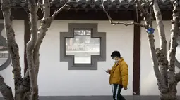 Seorang pria mengenakan masker melihat smartphone-nya saat dia berjalan di taman umum di Beijing, Rabu (5/1/2022). China melaporkan penurunan besar infeksi COVID-19 lokal di kota utara Xi'an, yang telah dikunci ketat selama dua minggu terakhir. (AP Photo/Mark Schiefelbein)