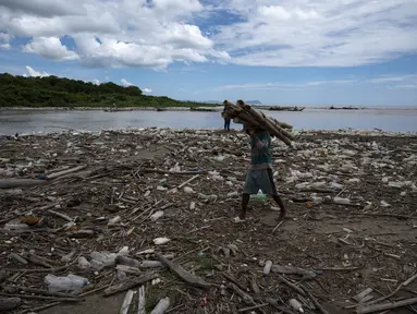 Seorang pria yang mengumpulkan bambu berjalan di antara sampah, termasuk sampah plastik, di Pantai Paparo di Negara Bagian Miranda, Venezuela, pada 6 Juni 2023. (Photo by Yuri CORTEZ / AFP)