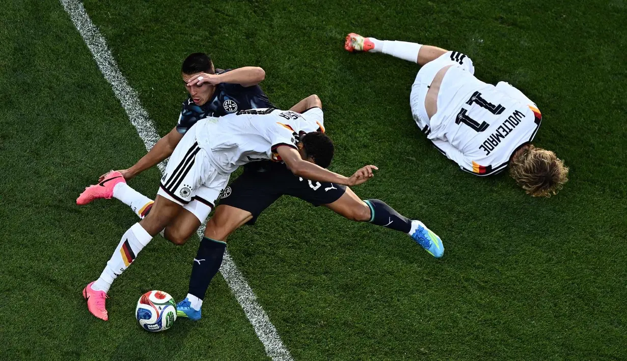 Pemain Jerman Jamal Musiala berebut bola dengan pemain Paraguay Braian Ojeda, sementara pemain Jerman, Nick Woltemade tergeletak di tanah selama pertandingan sepak bola babak 32 besar Piala Dunia 2026 antara Jerman dan Paraguay di Stadion Boston di Foxborough, AS, Senin (29/06/2026). AFP/ Jewel Samad