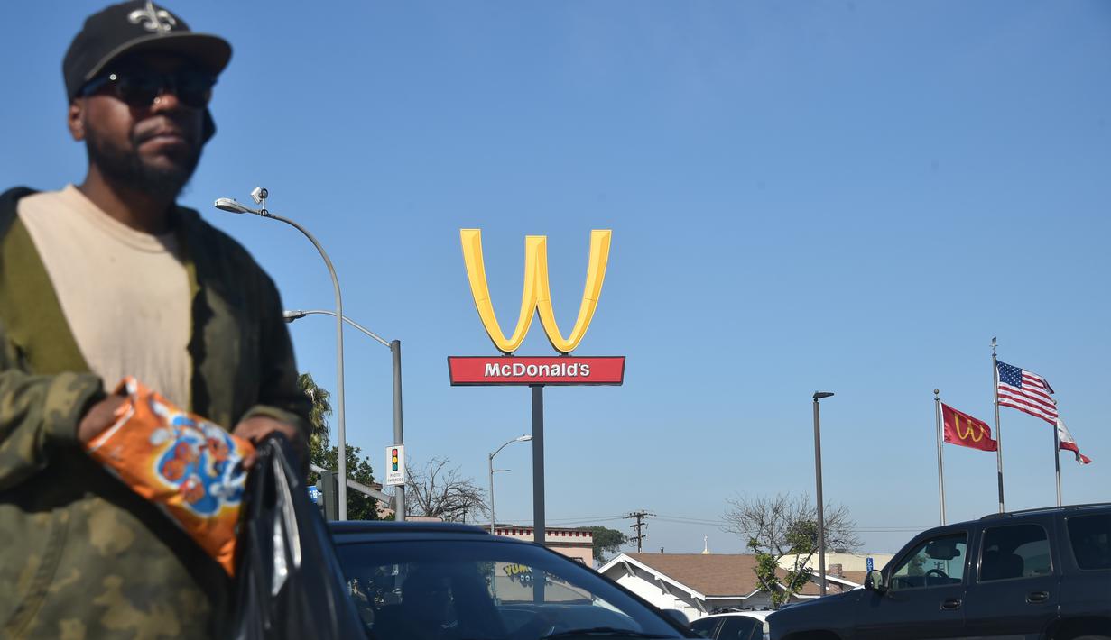 Seorang pria berjalan dengan latar belakang plang logo restoran McDonald's yang terbalik di Lynwood, California (8/3). Logo tersebut dibalik dari huruf M menjadi huruf W untuk peringati Hari Perempuan Internasional. (AFP Photo/Frederic J. Brown)