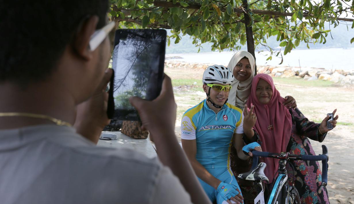 Warga sekitar Pantai Carocok berfoto bersama seorang pebalap sepeda berlomba dalam Etape 1 Tour de Singkarak antara Painan, Kabupaten Pesisir Selatan menuju Pariaman, Sumatra Barat saat, Sabtu (3/10/2015). (Bola.com/Arief Bagus)