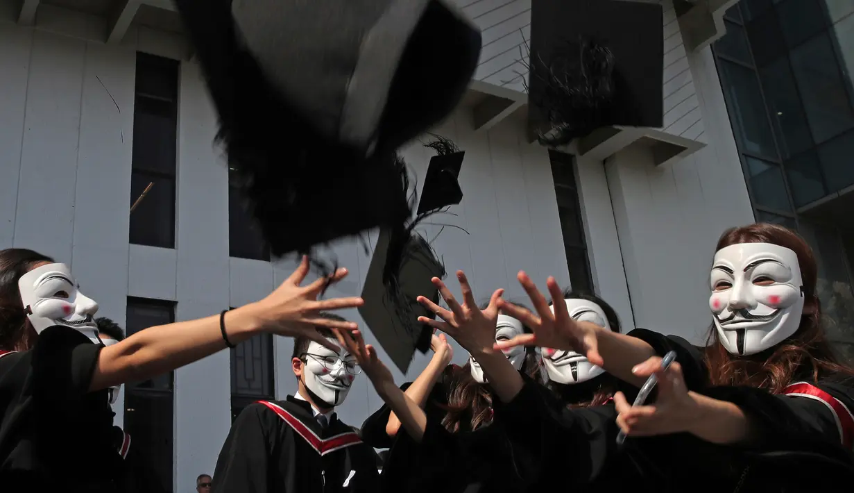 Wisudawan bertopeng Guy Fawkes melemparkan topi wisuda setelah upacara kelulusan mereka di Chinese University of Hong Kong, Hong Kong, Kamis (7/11/2019). Sekitar seribu mahasiswa mengabaikan larangan mengenakan topeng yang dikeluarkan pemerintah pada Oktober 2019. (AP/Kin Cheung)