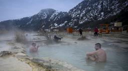 Orang-orang menikmati air panas di mata air mineral alami pada hari musim dingin di dekat desa Rupite, Bulgaria (2/2/2022). Penduduk setempat percaya bahwa air mineral menyembuhkan banyak penyakit dan gangguan. (AFP/Nikolay Doychinov)