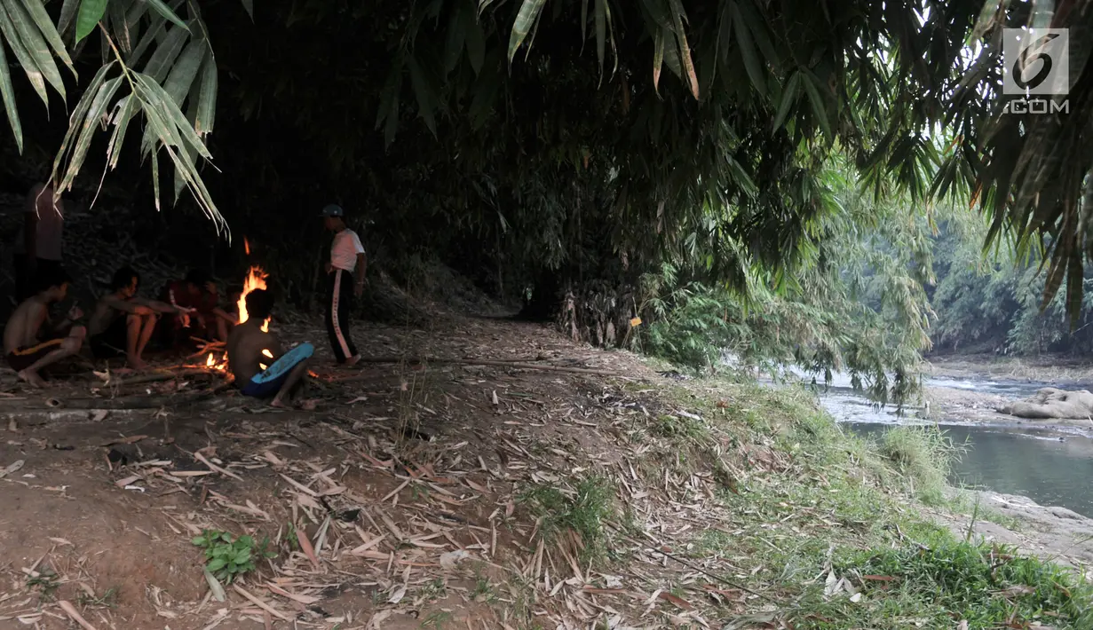 Anak-anak membakar ranting pohon saat jeda berenang di Sungai Ciliwung, Depok, Jawa Barat, Kamis (4/7/2019). Menurunnya debit air Sungai Ciliwung akibat musim kemarau dimanfaatkan warga setempat sebagai tempat wisata gratis untuk mengajak anak berenang. (merdeka.com/Iqbal Nugroho)