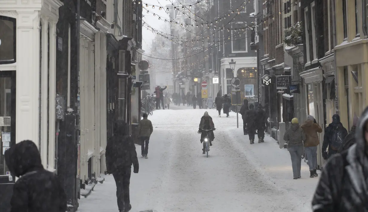 Seorang wanita mengendarai sepedanya di pusat kota Amsterdam, ketika salju dan angin kencang menyelimuti sebagian besar wilayah Belanda, Minggu (7/2/2021). Badai salju dengan suhu mencapai minus 10 derajat celsius membuat transportasi umum tidak beroperasi. (AP Photo/Peter Dejong)