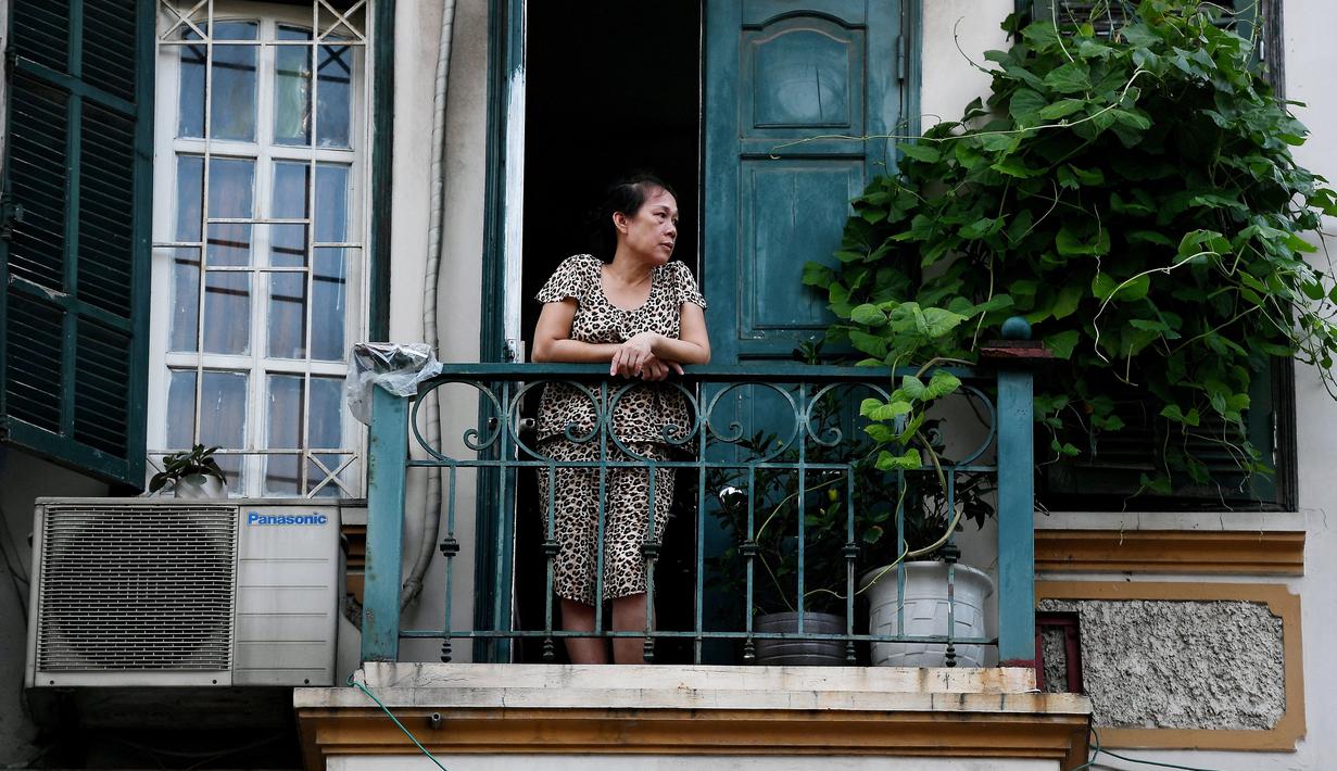 Gambar pada 2 September 2021 menunjukkan seorang perempuan melihat keluar dari balkon rumahnya di Hanoi, Vietnam, selama lockdown Covid-19. Menghadap ke jalan yang sepi, balkon kecil mereka menjadi saksi bisu terkait aktivitas yang dilakukan oleh masing-masing keluarga. (Nhac NGUYEN/AFP)