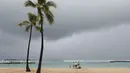 Para pengunjung pantai terlihat dengan latar belakang awan badai, di Pantai Waikiki, Honolulu  (6/12/2021). Badai kuat yang membawa angin kencang dan hujan yang sangat deras membanjiri jalan-jalan dan meruntuhkan kabel listrik dan cabang-cabang pohon di seluruh Hawaii. (AP Photo/Marco Garcia)