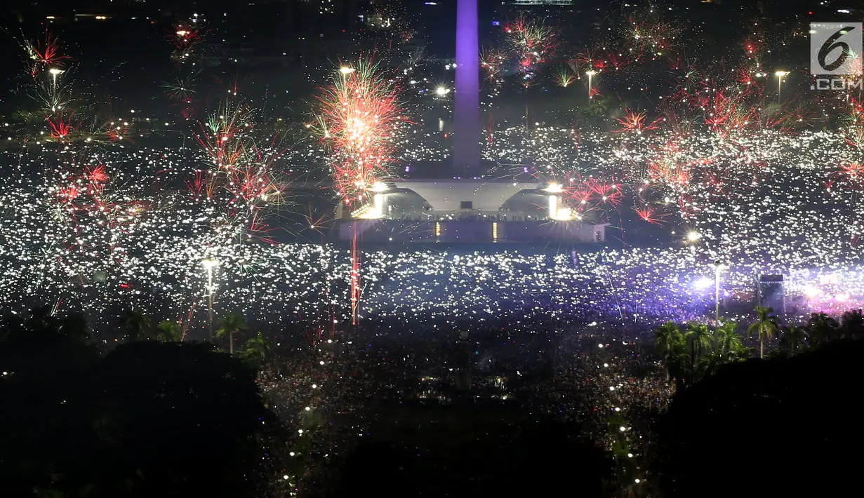 Ribuan warga mengabadikan moment kembang api pada malam pergantian tahun baru 2018 di kawasan silang Monumen Nasional (Monas), Jakarta, Senin (1/1/2018). Monas menjadi salah satu lokasi pilihan warga saat malam tahun baru. (Liputan6.com/Johan Tallo)
